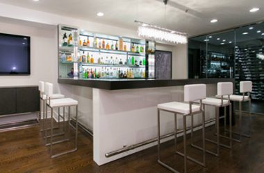 Luxury modern home bar by Weizter featuring a sleek white bar counter, illuminated back bar shelving, contemporary bar stools and a sophisticated entertainment setting.