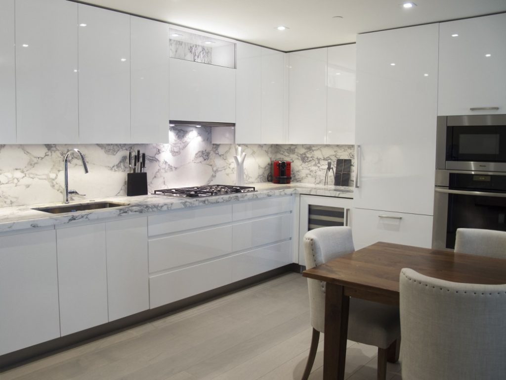 White high-gloss kitchen cabinets with stone-effect countertops and backsplash