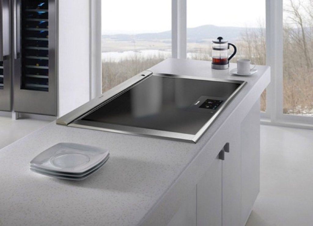 Kitchen island with built-in black glass hob, white countertop, and stacked plates