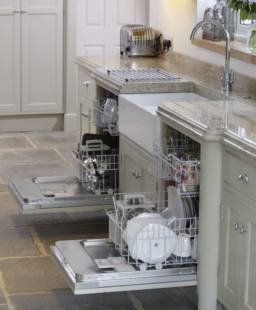 Open dishwashers integrated into kitchen cabinetry with stone floor and countertop
