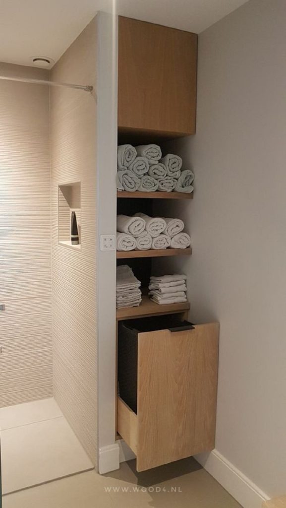 Wooden bathroom storage unit with open shelves holding rolled white towels and a pull-out drawer