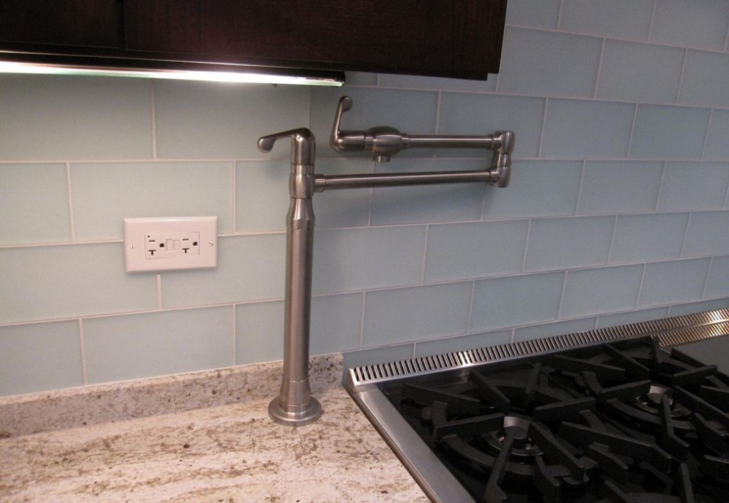 Stainless steel pot filler tap mounted on kitchen countertop near gas stove and tiled backsplash