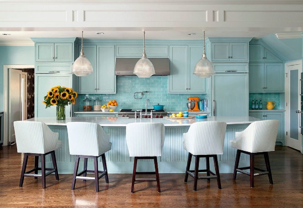 Light blue kitchen cabinetry with white bar stools and pendant lights over island