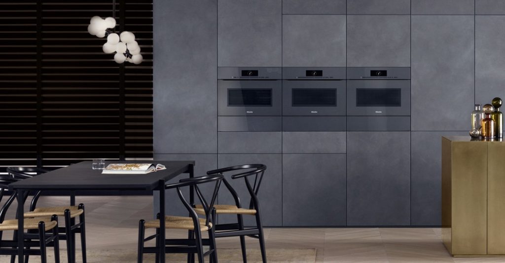 Built-in kitchen appliances integrated into grey cabinetry with black dining table and chairs
