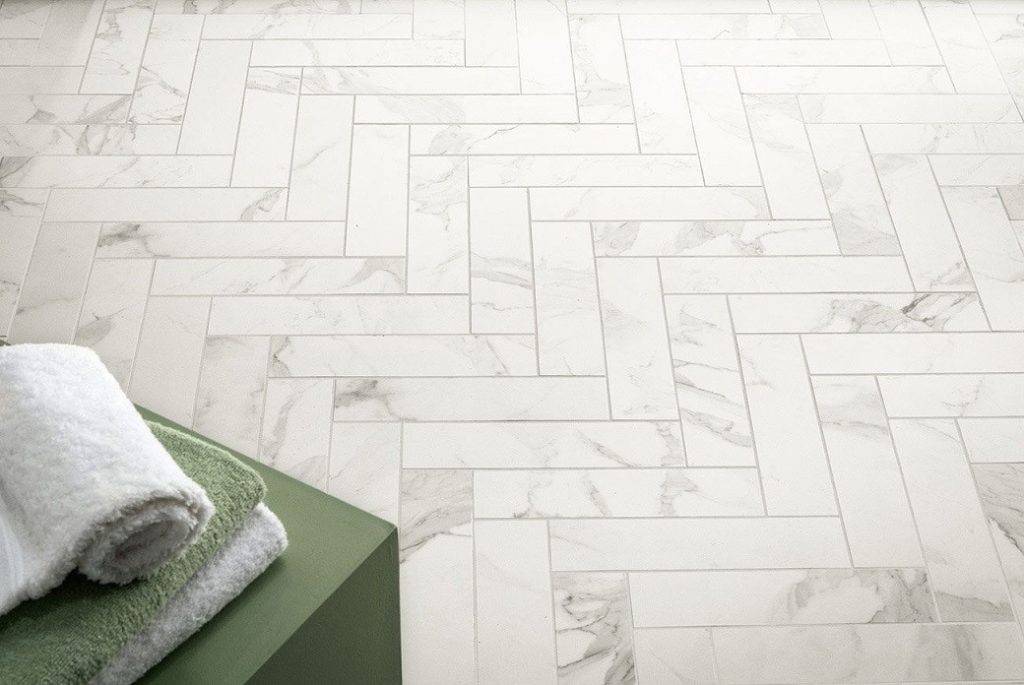 White stone-effect floor tiles laid in a herringbone pattern with folded towels on a green surface