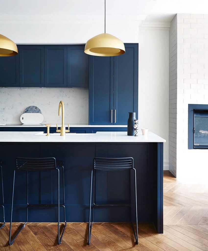 Kitchen with dark blue cabinetry, white countertop, gold pendant lights and wooden herringbone floor