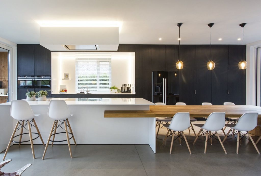 Bright kitchen with white island, wooden dining table, white chairs and black cabinetry