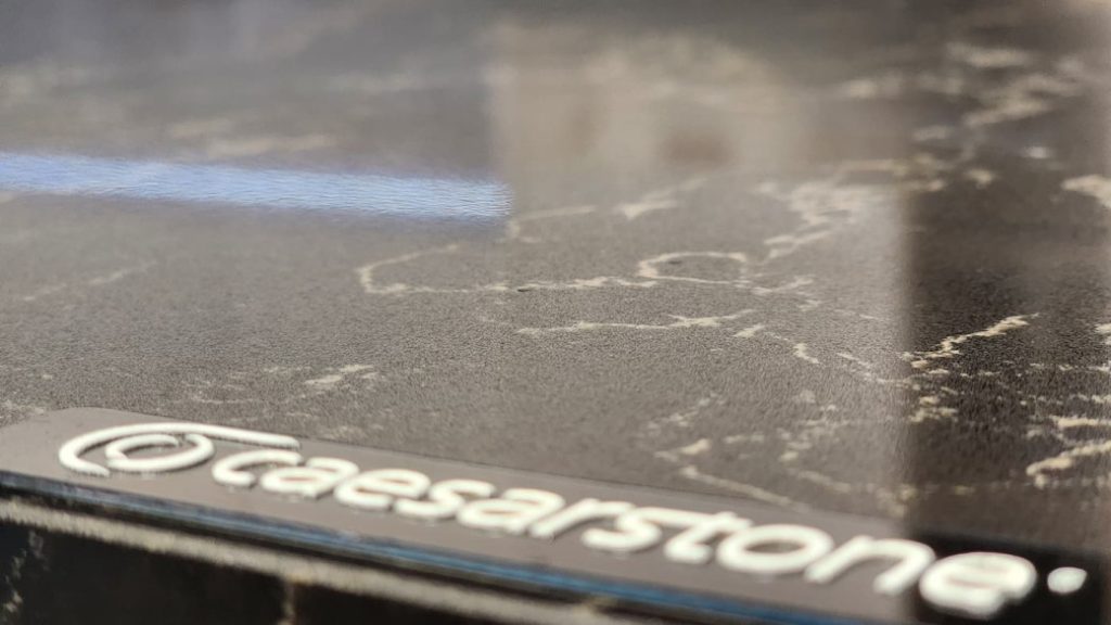 Close-up of a dark stone kitchen countertop with light veining and Caesarstone logo