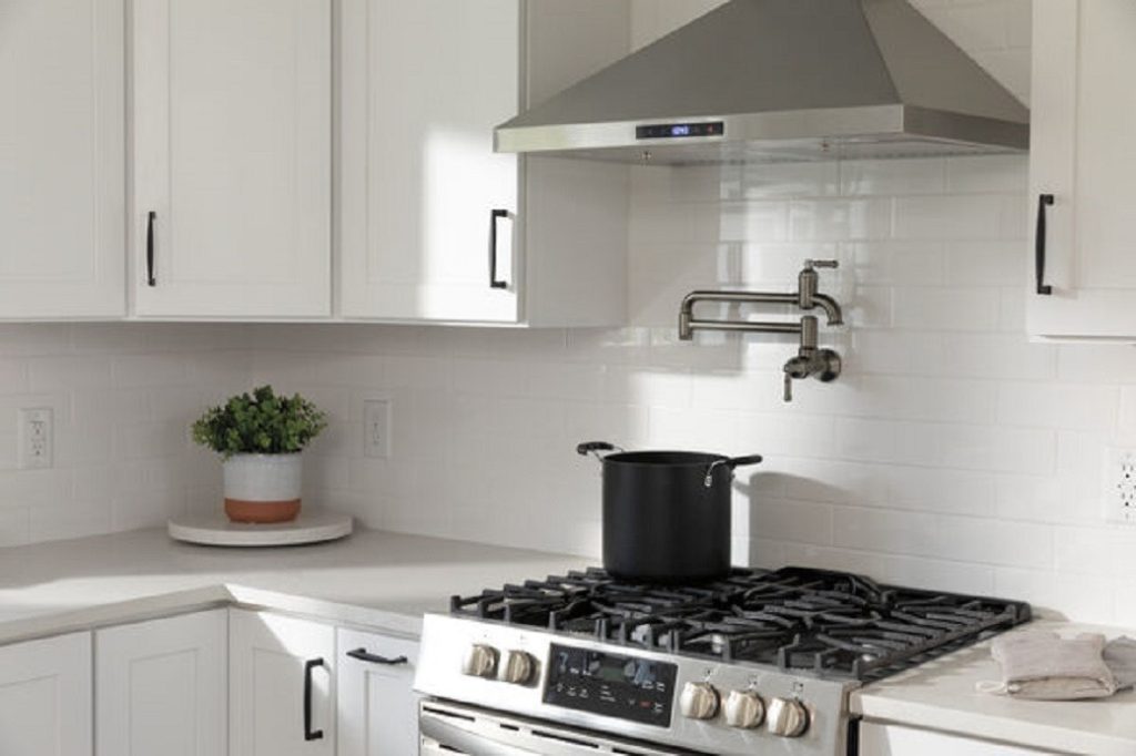 Black pot on stainless steel gas stove with white cabinetry and pot filler tap