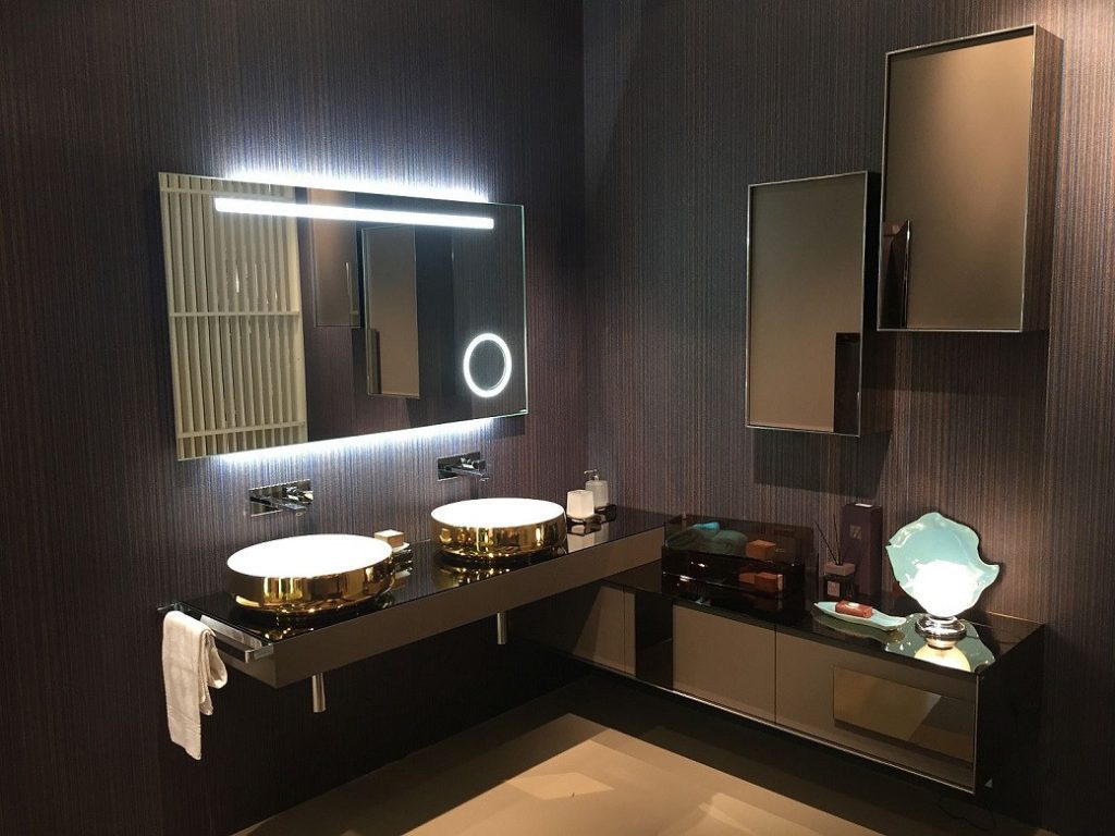 Bathroom vanity with two round gold-coloured basins on black countertop and illuminated mirror
