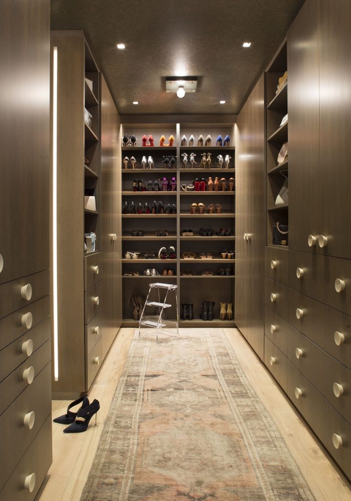 Walk-in closet with wooden shelves and cabinets filled with shoes and handbags