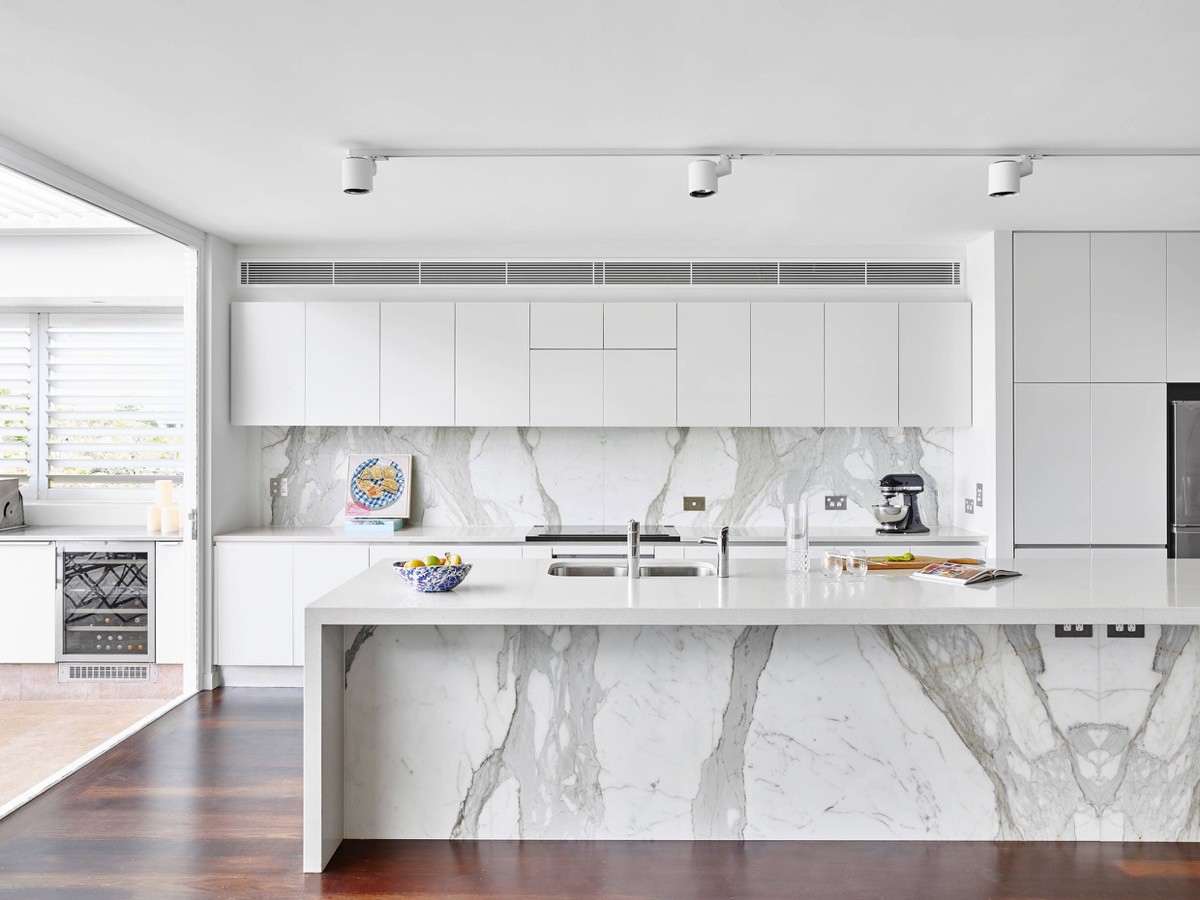 Minimalist modern kitchen with white handleless cupboards, bold red base cabinets, stainless steel extractor and a white dining area.
