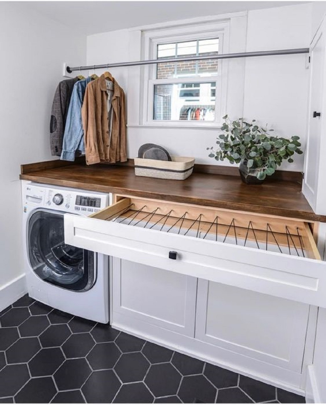Laundry room with black hexagon floor tiles, white cabinets, wooden countertop, open clothes drying drawer, clothes hanging r
