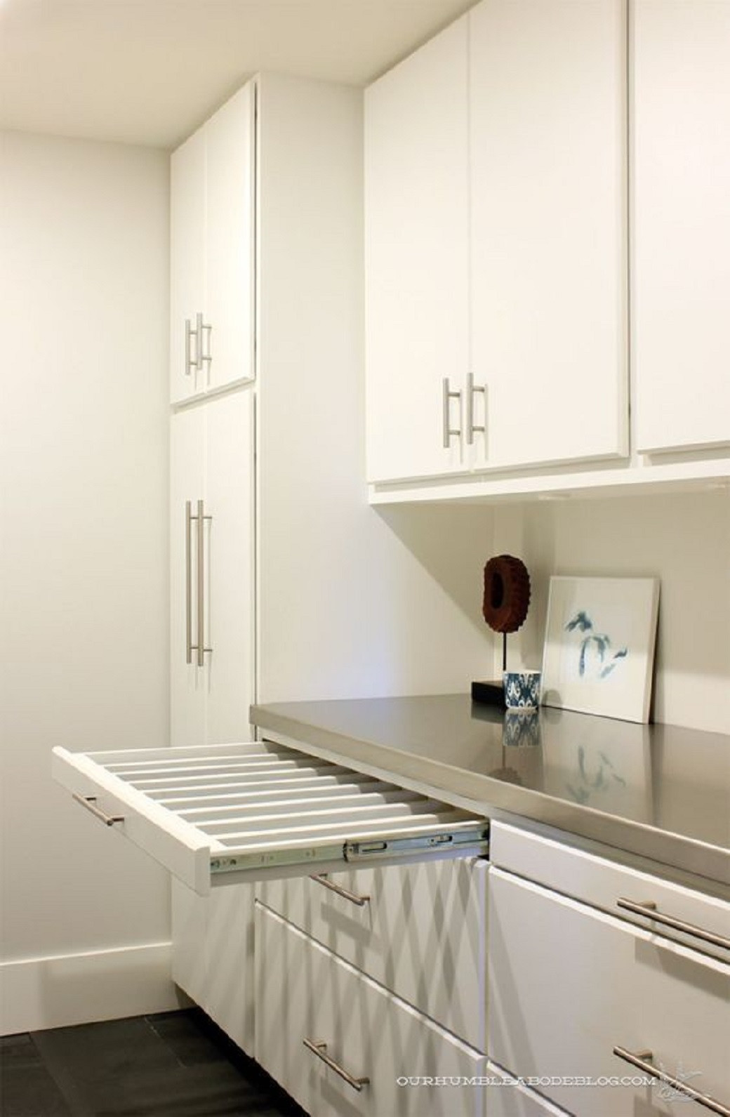White scullery with multiple cabinets, a metal countertop, and a pull-out drying rack drawer extended.