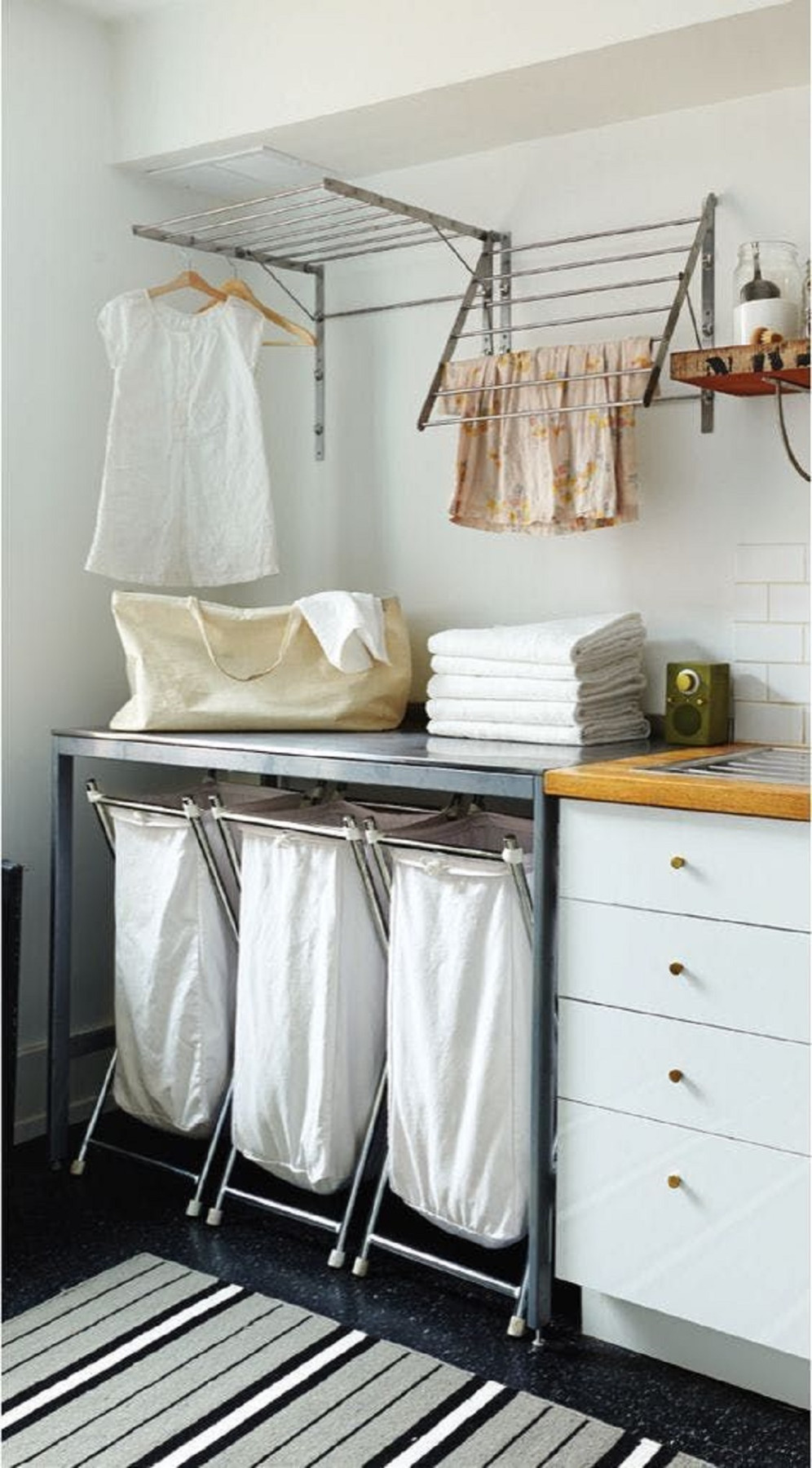 Laundry room with three fabric laundry bags on a metal frame, folded towels on a black table, and clothes drying on wall-moun