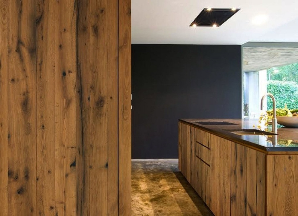 Modern kitchen with wooden cabinetry and island, black countertop, built-in sink, minimalist ceiling light, and large window.