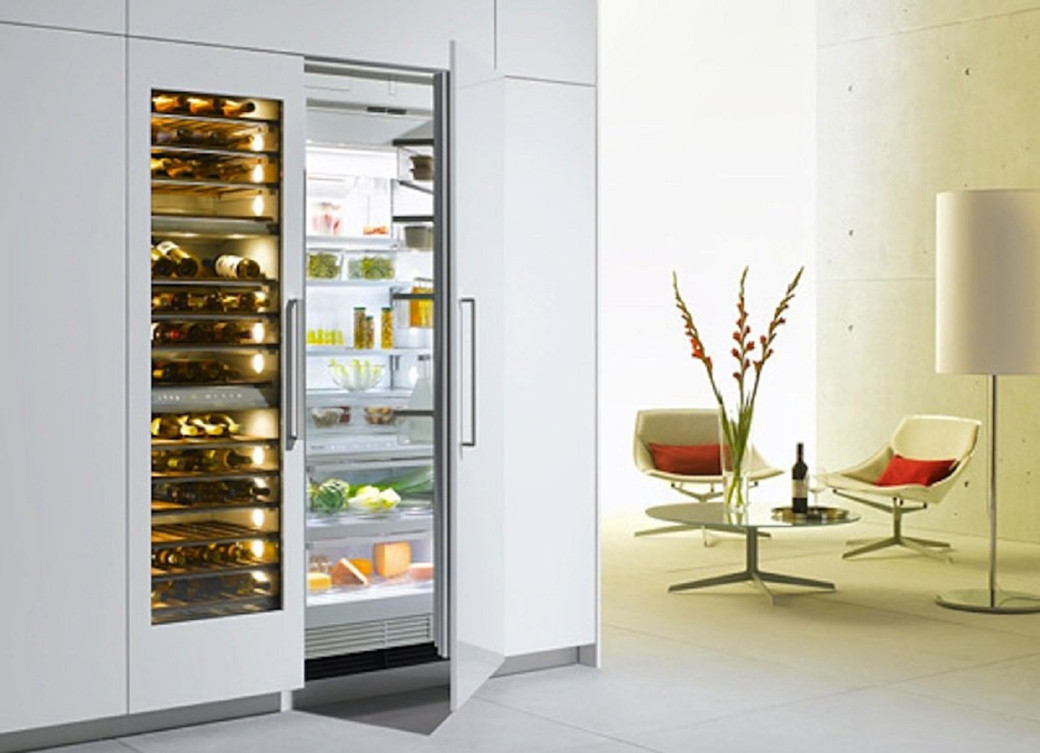 Modern kitchen scene with a built-in fridge and wine cooler, two chairs, a round table, flowers, and a floor lamp.