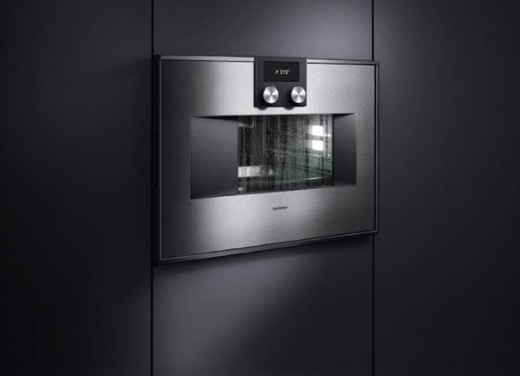 Built-in stainless steel oven with digital display and two control knobs set into a dark matte kitchen cabinet.