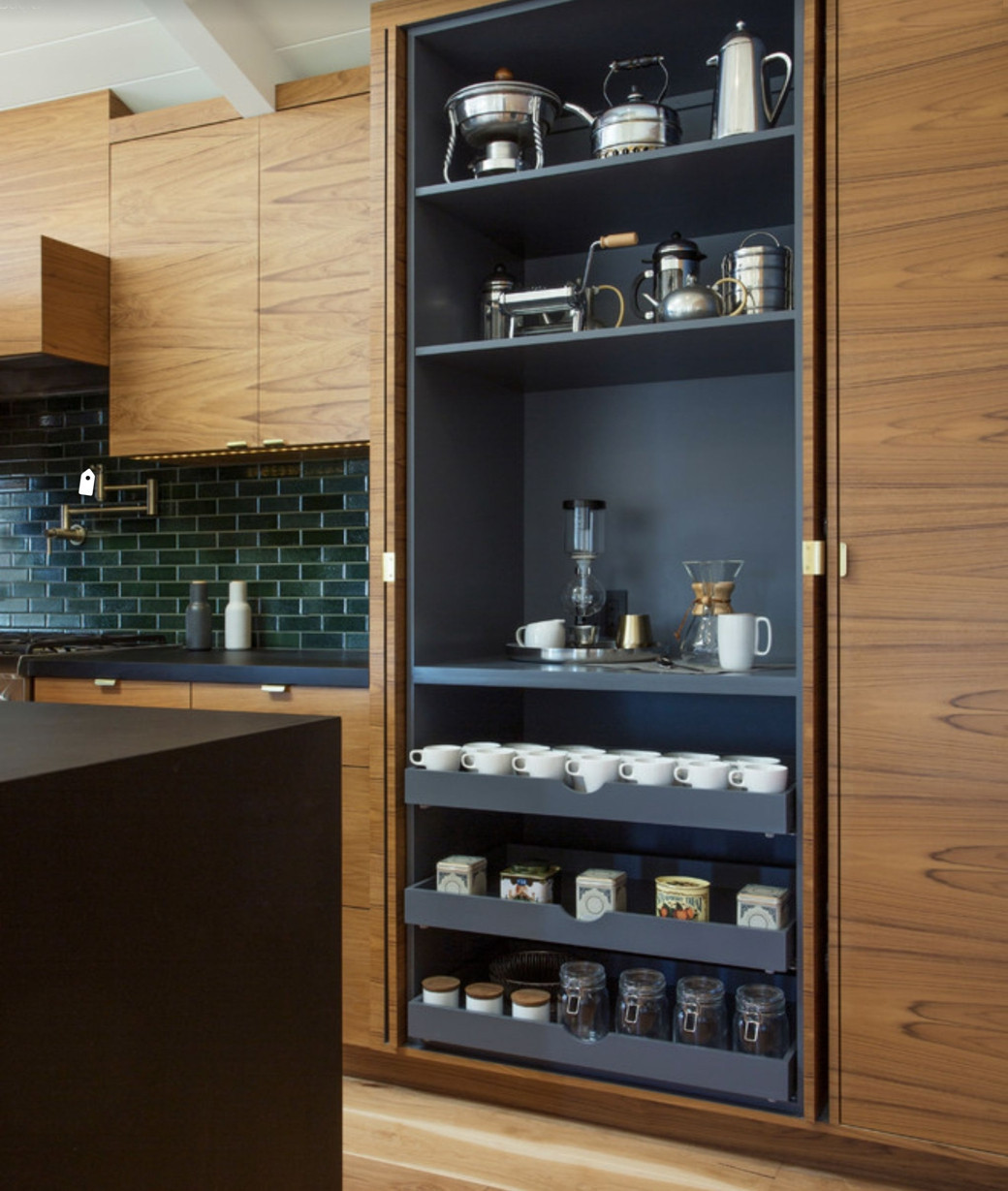 Tall wooden cabinet open to reveal a built-in coffee station with mugs, jars, tins, and coffee-making equipment.