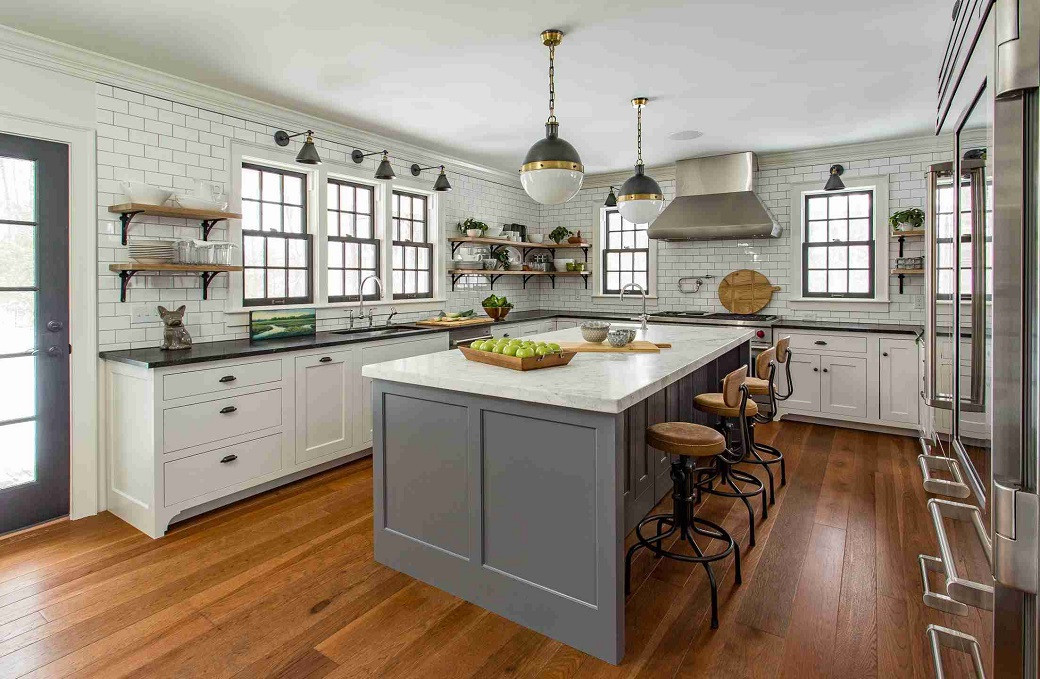 Spacious farmhouse kitchen with white cabinets, large grey island, wooden stools, subway tile backsplash, and hardwood floors
