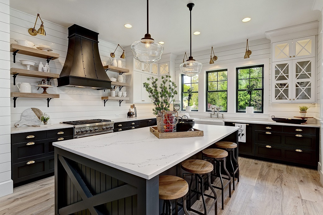 Farmhouse kitchen with black lower cabinets, white upper cabinets, wood shelving, large island with stools, and pendant light