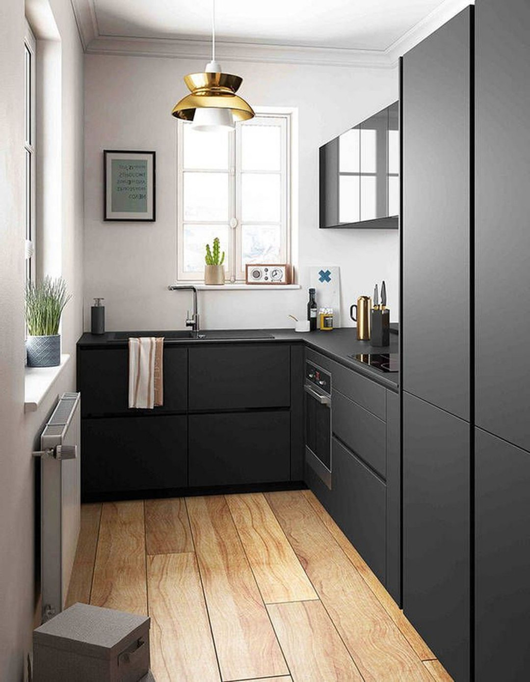 Small modern kitchen with black cabinets, wooden floor, window, gold pendant light, and small plants on the windowsill.
