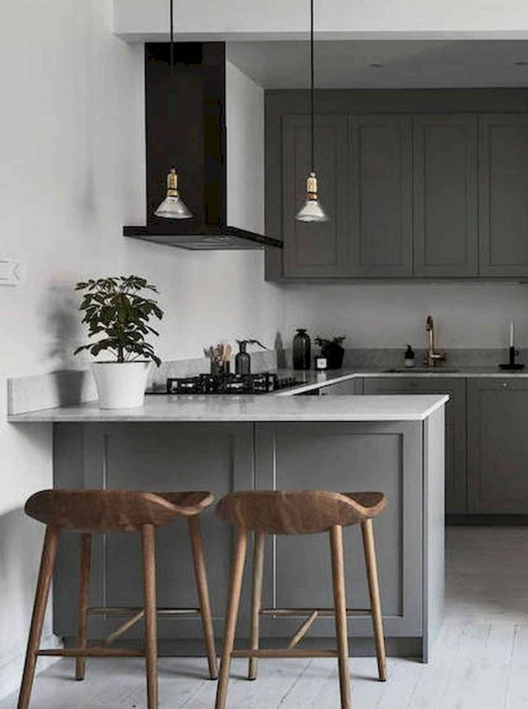 Small kitchen with grey cabinetry, marble countertop, wooden stools, pendant lights, and a potted plant.