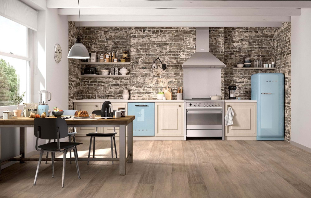 Open-plan kitchen with exposed brick wall, light wood flooring, pastel blue retro fridge and dishwasher, wooden table with bl
