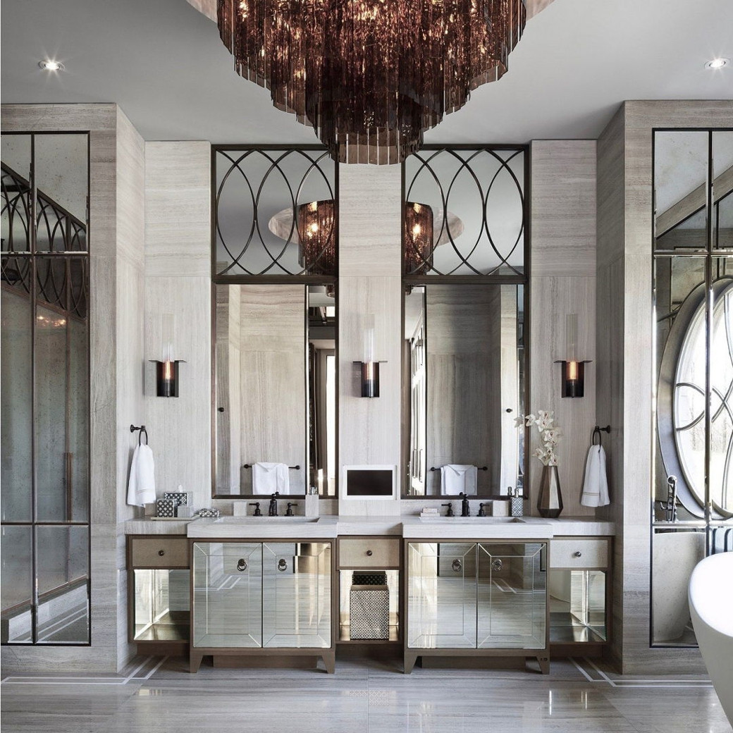 Luxury bathroom with twin mirrored vanities, large vertical mirrors with decorative upper panels and a central chandelier.