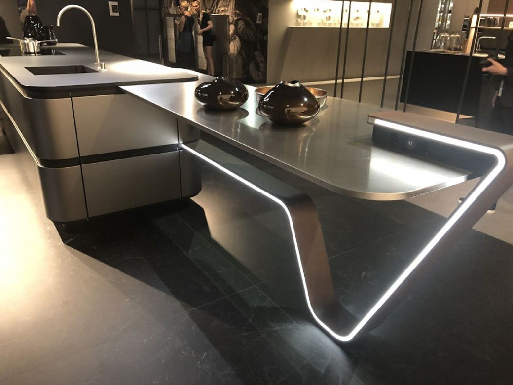 Sleek modern kitchen island with integrated sink and curved LED-lit table extension, dark floor and background.