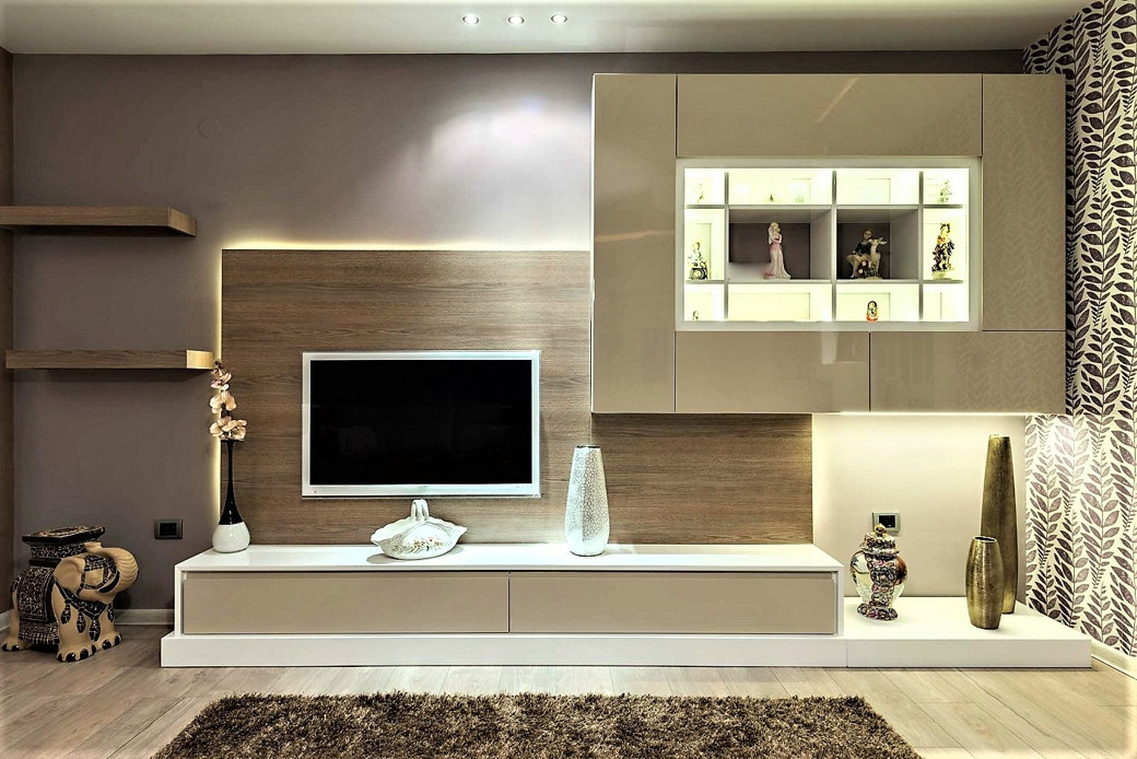 Modern TV cabinet with glossy beige drawers, wood panel backdrop, decorative shelves, vases, and figurines.