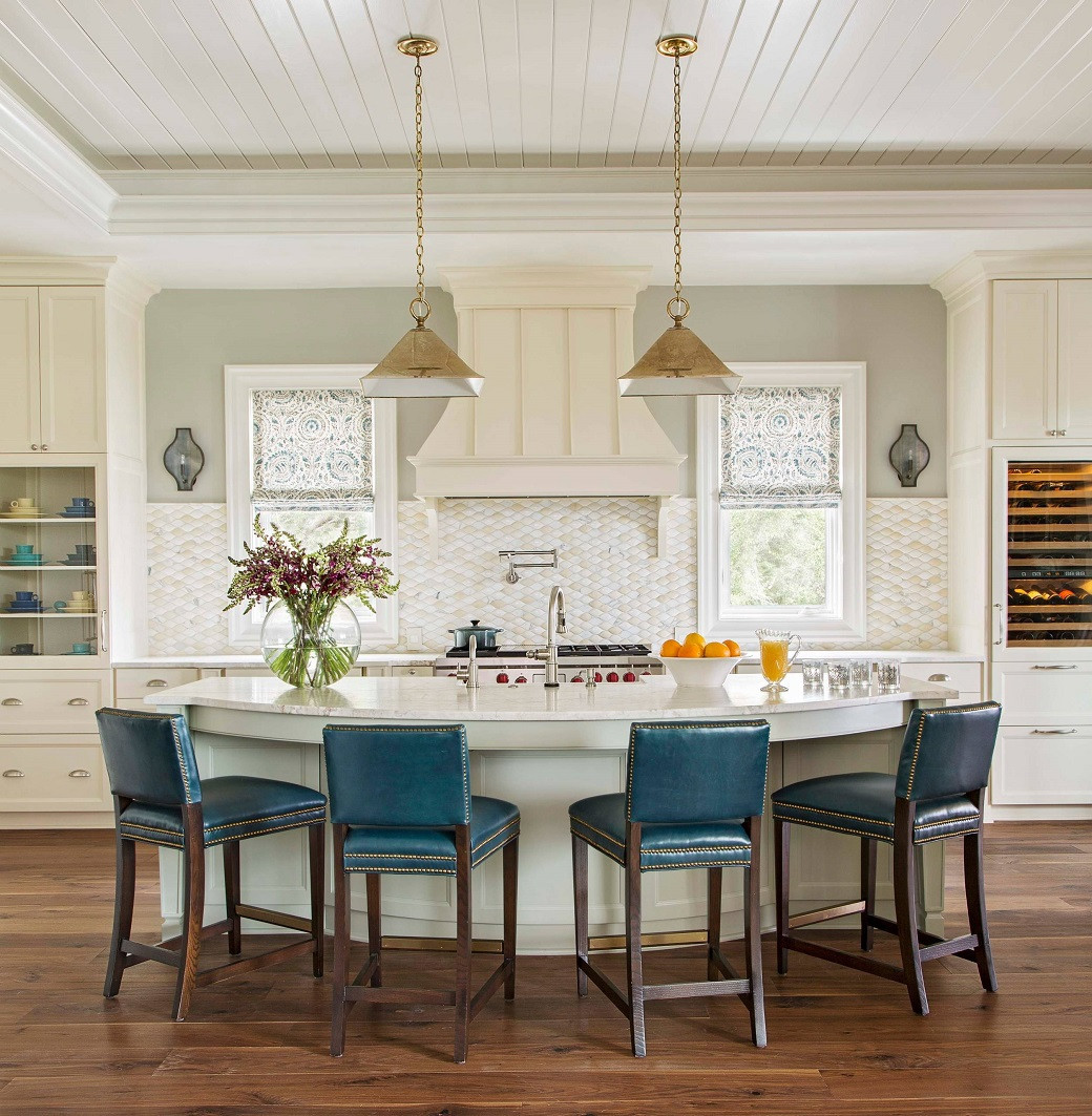 Modern kitchen with a curved white island, five blue bar stools, pendant lights, and floral arrangements on a wooden floor.