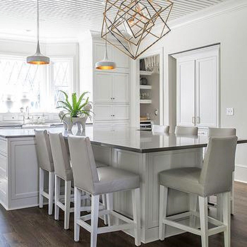 Modern white kitchen with a large rectangular island, six high-back padded stools, and pendant lights.