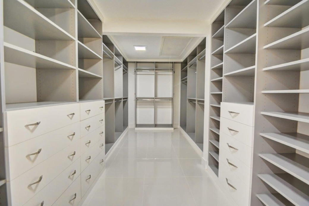 Empty walk-in closet with multiple white shelves, drawers, and hanging rods on both sides.