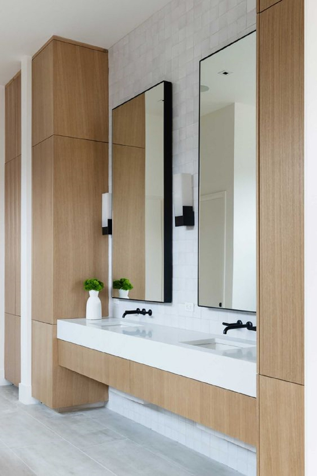 Modern bathroom with double sink vanity, wood cabinetry, large rectangular mirrors, and a small white vase with green plant.