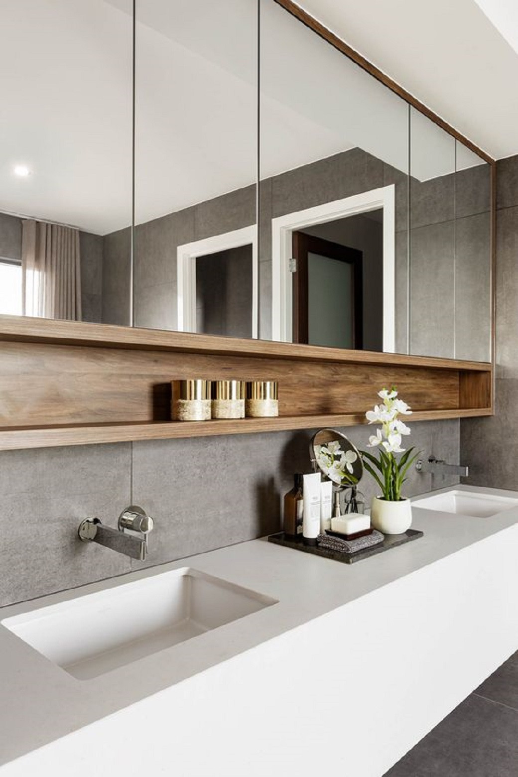 Modern bathroom with dual rectangular sinks, wall-mounted taps, large mirrors, wooden shelf with jars, and decorative orchids