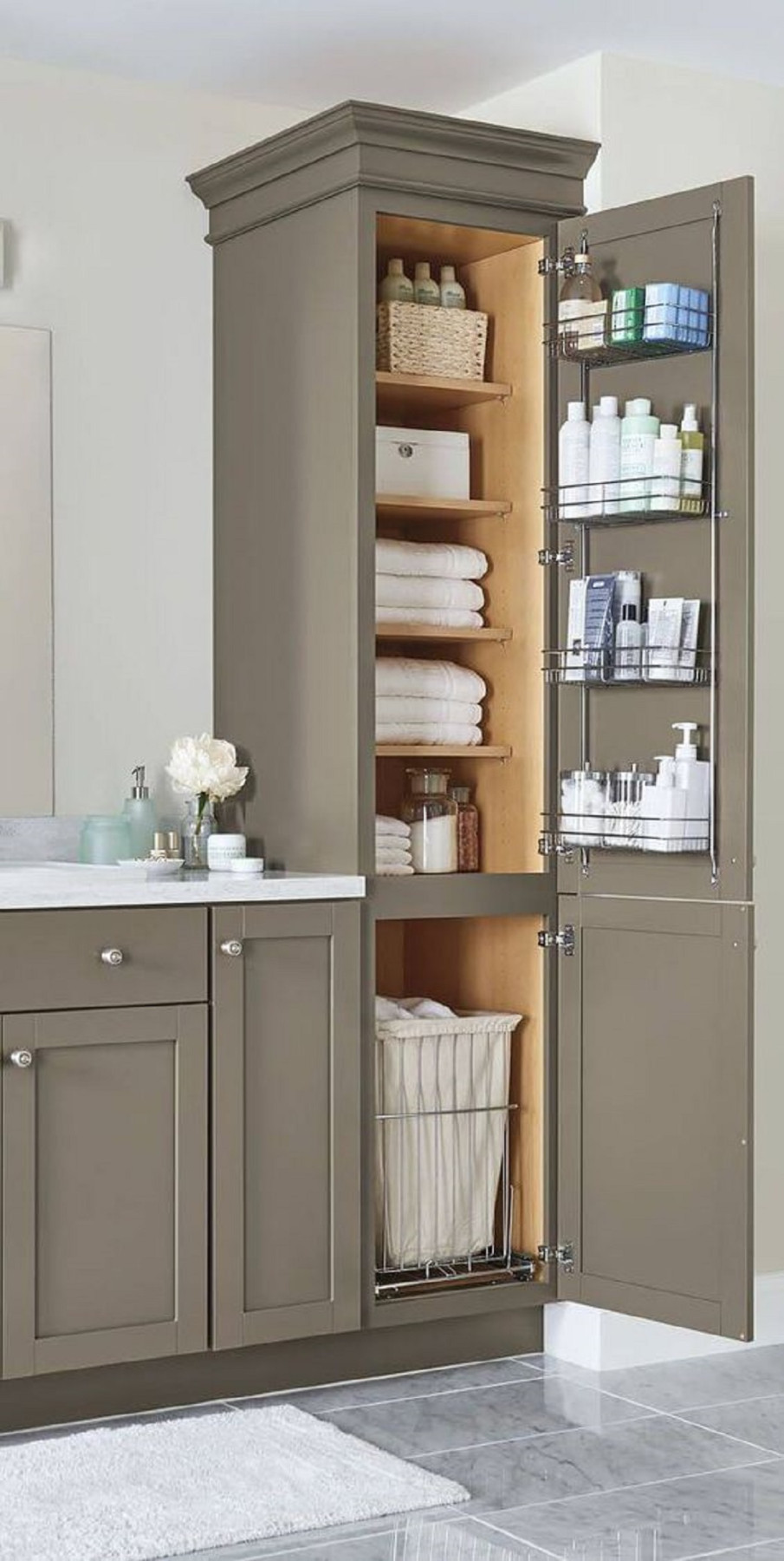 Bathroom cabinet with open door showing neatly folded towels, storage baskets, toiletries on racks, and a laundry hamper.