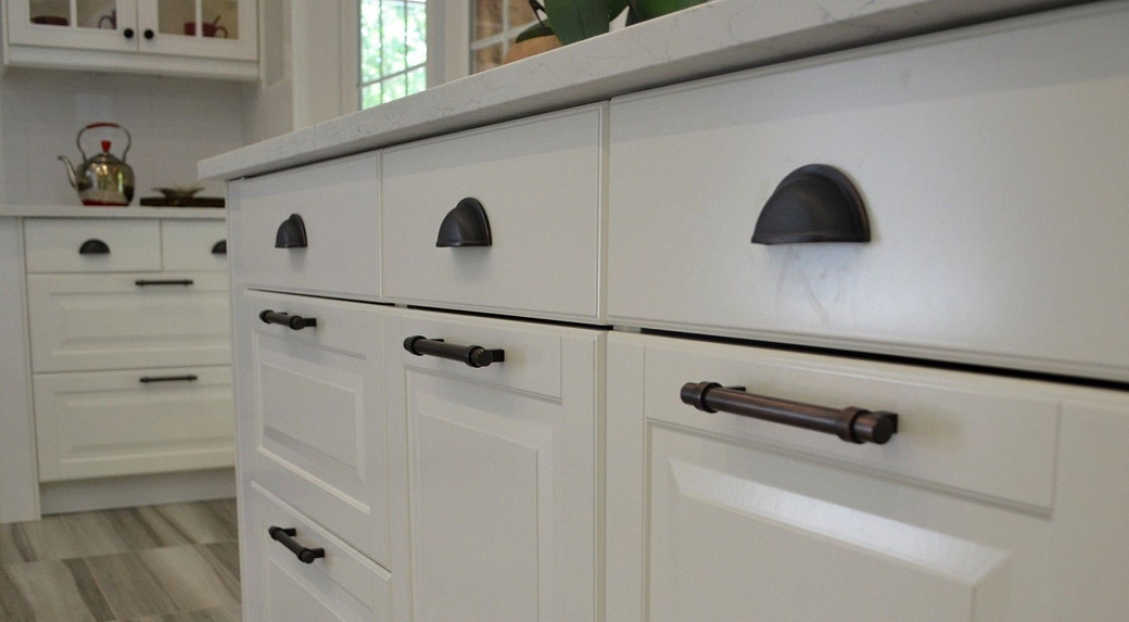 Close-up of white kitchen cabinets with dark bronze cup pulls on drawers and bar handles on cupboard doors.