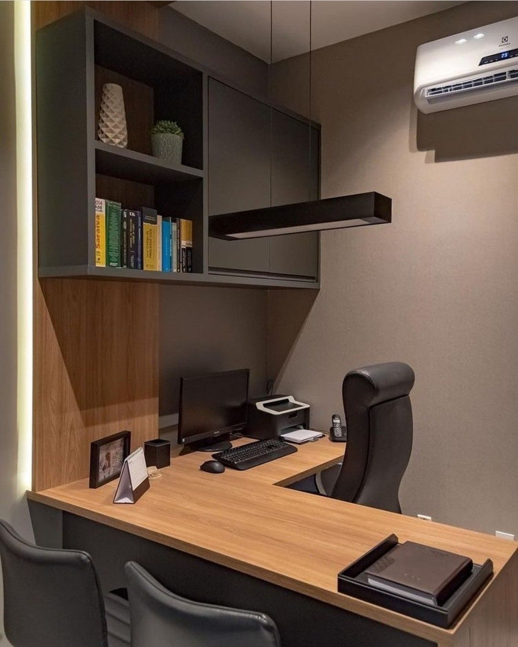 Compact home office with wooden desk, black office chair, computer, printer, shelves with books and decor, and wall-mounted a