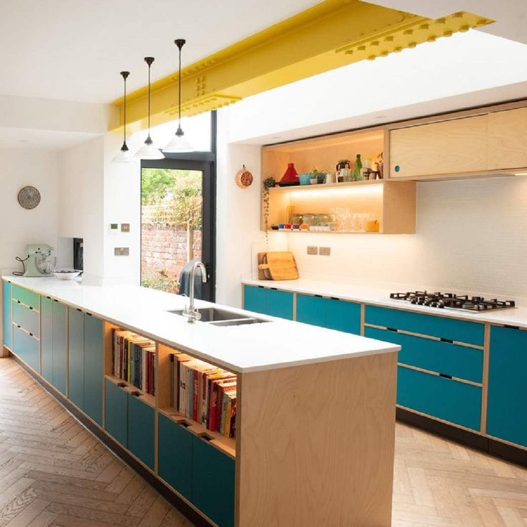 Kitchen with teal cabinets, white countertops, open shelves with lights, yellow ceiling beam, and wooden herringbone floor.
