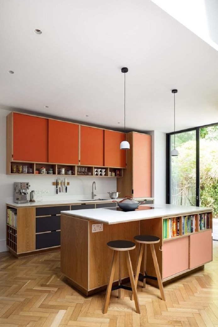 Modern kitchen with orange and black cabinets, wooden island with built-in bookshelf, two stools, and pendant lights.