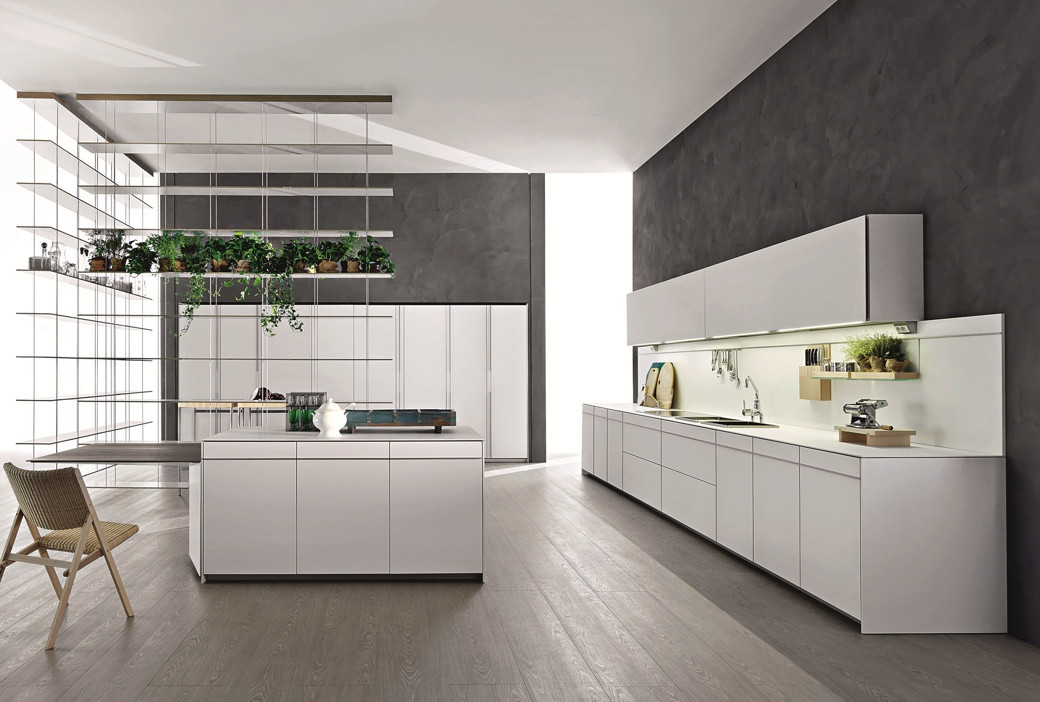 Modern white kitchen with island, minimalist cabinets, hanging plants, grey walls, wooden chair, and light wood flooring.