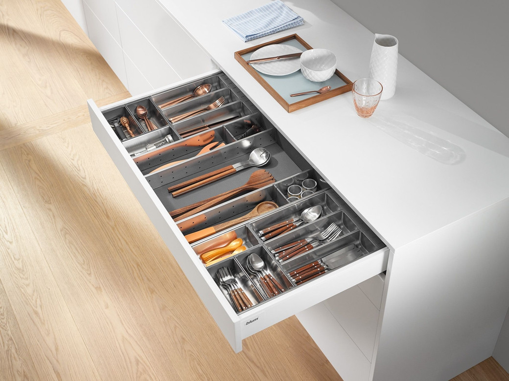 Open white kitchen drawer with organised compartments holding wooden and metal cutlery and kitchen utensils.