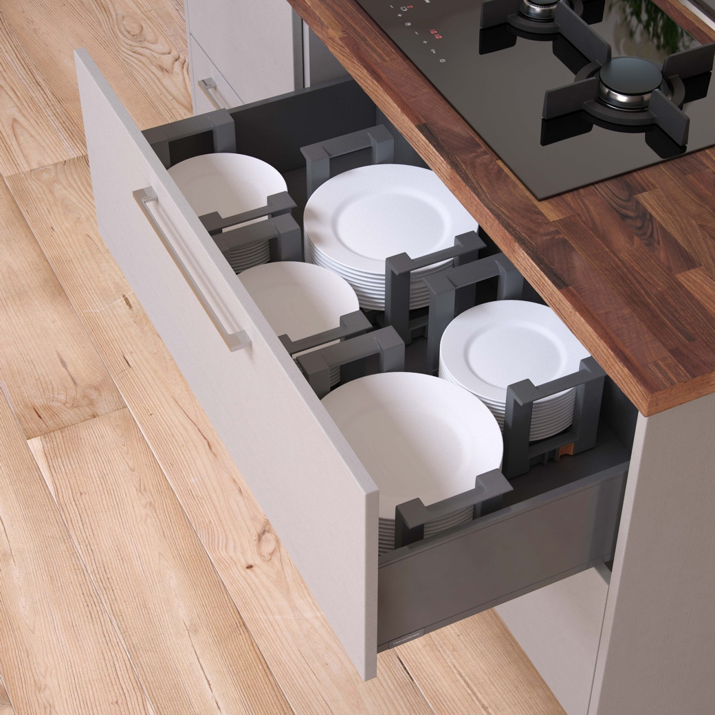 Open kitchen drawer with organised white plates secured by adjustable grey dividers under wooden countertop with gas stove.