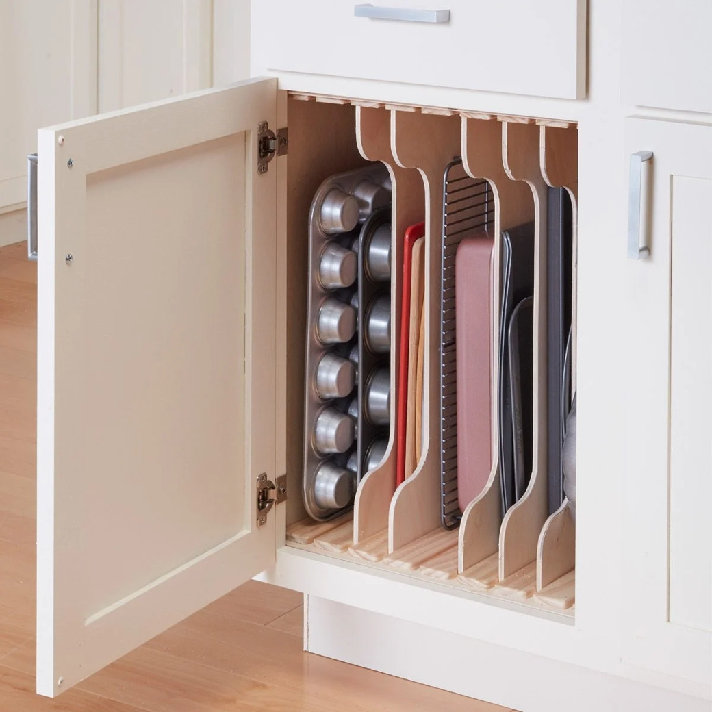 Open kitchen cabinet door revealing vertical wooden dividers storing baking trays and pans upright.