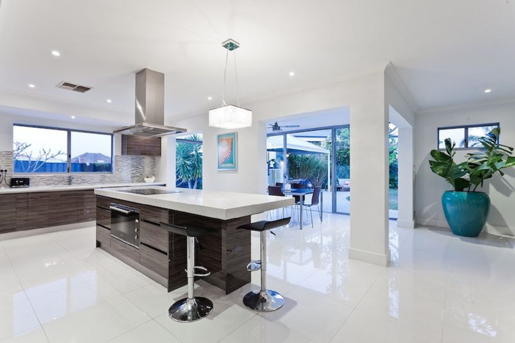 Modern kitchen with white tiled floor, dark wood cabinets, central island with stools, and large windows opening to patio.