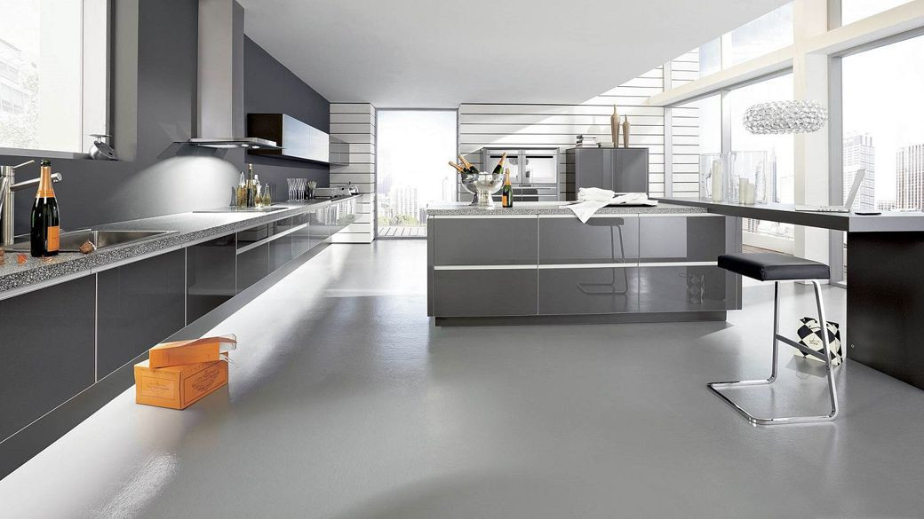 Modern kitchen with sleek grey cabinetry, large island, polished concrete floor, and cityscape visible through tall windows.