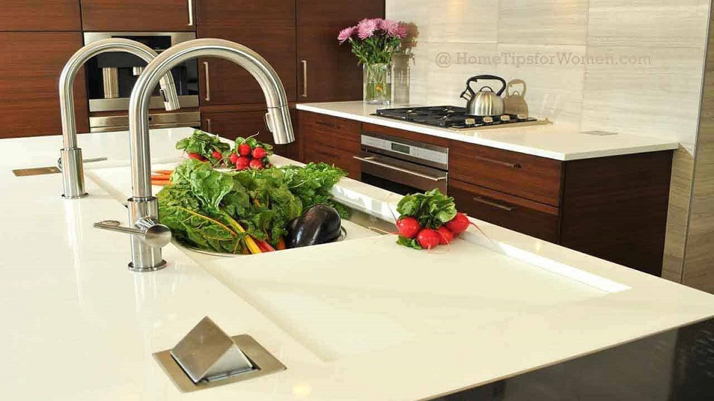 Modern kitchen countertop with built-in sink holding fresh greens and radishes, stainless steel taps, and a stove with a kett