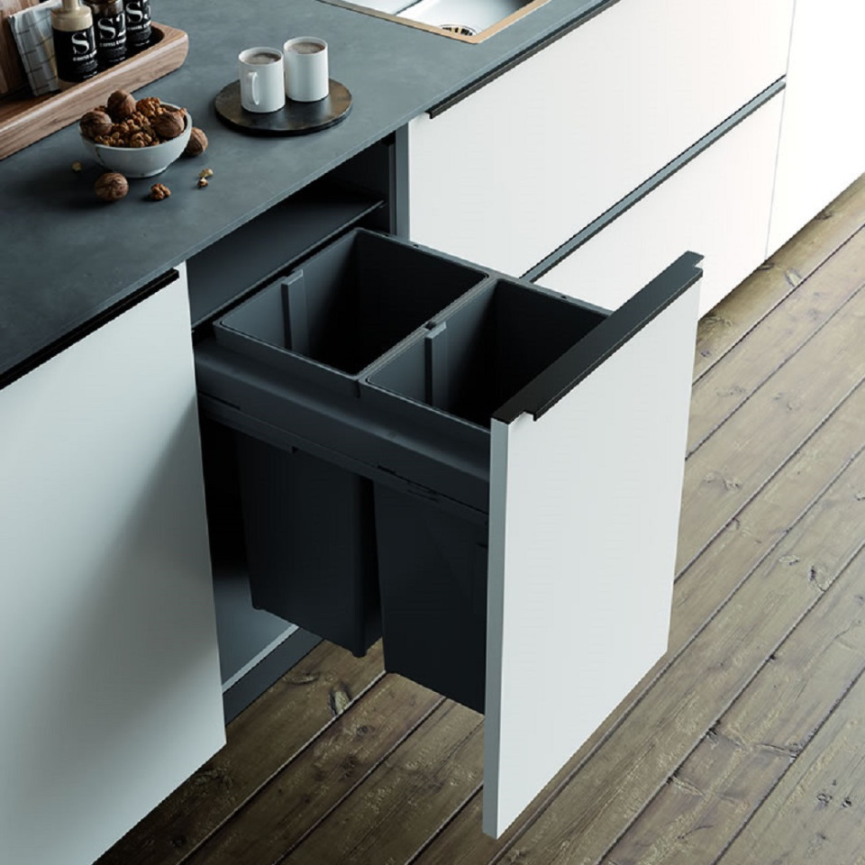 Modern kitchen cabinet with pull-out dual black waste bins, black countertop, and wooden floorboards.