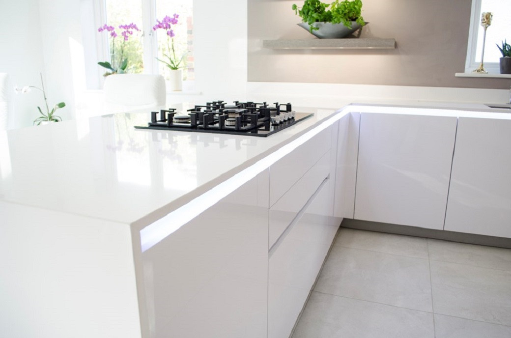 Modern white kitchen with glossy cabinets, built-in gas stove, and potted plants on windowsill and shelf.
